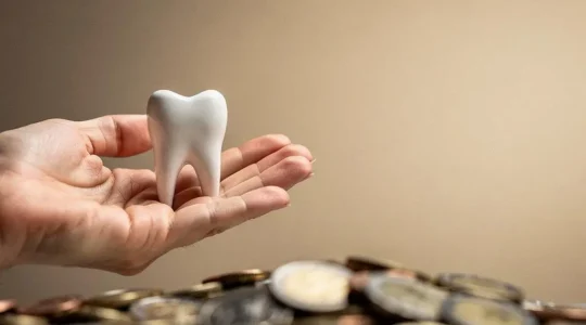 Une main tenant délicatement une dent stylisée en céramique entourée de pièces de monnaie floutées, symbolisant le financement d'un implant dentaire